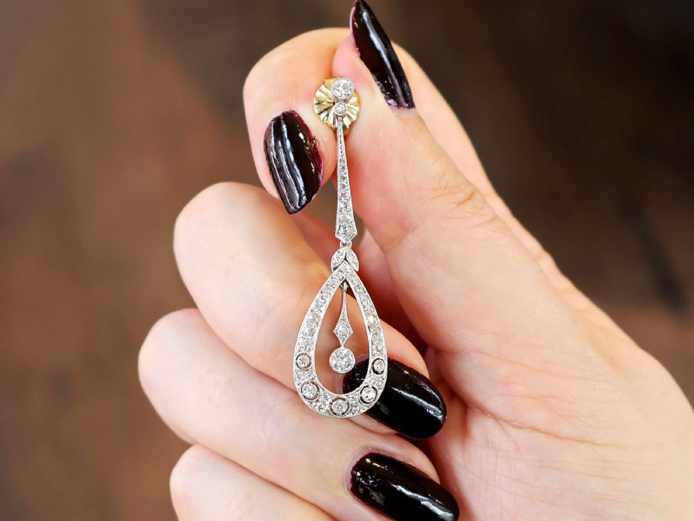 A pair of Art Deco platinum drop earrings featuring openwork teardrop frames set with diamonds and geometric articulated tops. View III