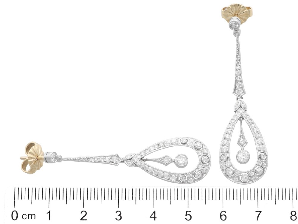 A pair of Art Deco platinum drop earrings featuring openwork teardrop frames set with diamonds and geometric articulated tops. View VII