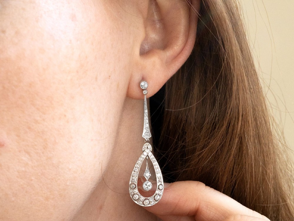 A pair of Art Deco platinum drop earrings featuring openwork teardrop frames set with diamonds and geometric articulated tops. View IX