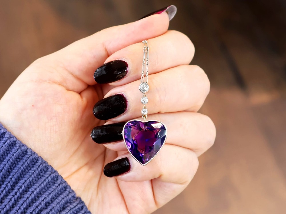 An antique heart-cut purple amethyst pendant framed with a millegrain edge and suspended beneath three round diamond accents set in gold. View IV