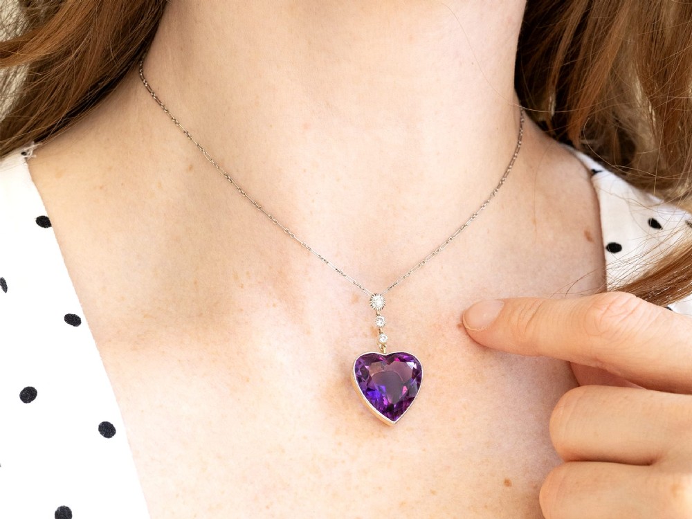 An antique heart-cut purple amethyst pendant framed with a millegrain edge and suspended beneath three round diamond accents set in gold. View VII
