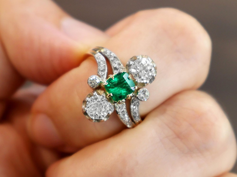 An antique 18ct yellow gold twist ring set with a central green emerald, flanked by two old cut diamonds and diamond-set shoulders. View III