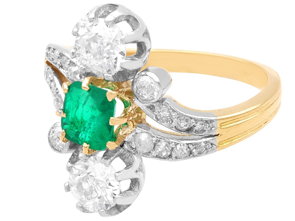 An antique 18ct yellow gold twist ring set with a central green emerald, flanked by two old cut diamonds and diamond-set shoulders. View VII
