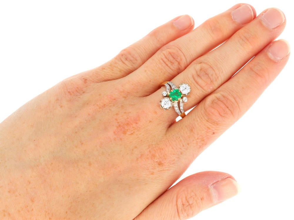An antique 18ct yellow gold twist ring set with a central green emerald, flanked by two old cut diamonds and diamond-set shoulders. View XI