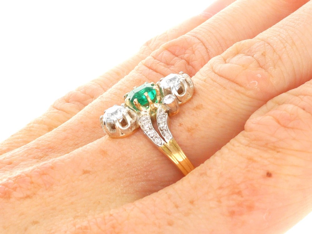 An antique 18ct yellow gold twist ring set with a central green emerald, flanked by two old cut diamonds and diamond-set shoulders. View XII