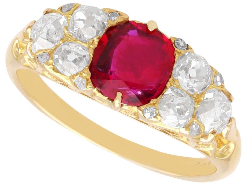 An 18ct yellow gold dress ring featuring a central cushion-cut red ruby flanked by old cut diamonds with carved scrollwork setting.