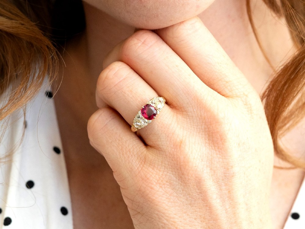 An 18ct yellow gold dress ring featuring a central cushion-cut red ruby flanked by old cut diamonds with carved scrollwork setting. View III
