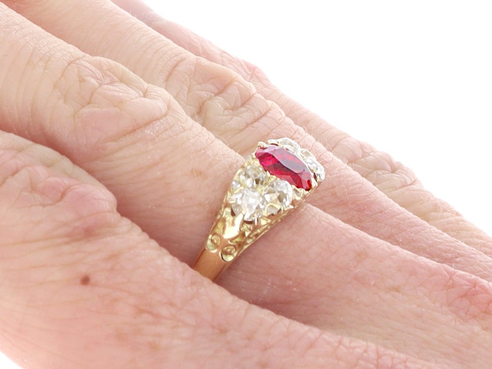An 18ct yellow gold dress ring featuring a central cushion-cut red ruby flanked by old cut diamonds with carved scrollwork setting. View IX