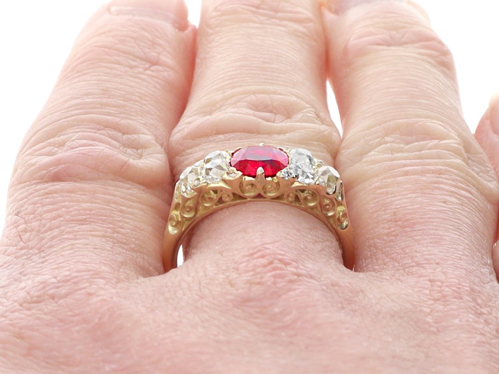 An 18ct yellow gold dress ring featuring a central cushion-cut red ruby flanked by old cut diamonds with carved scrollwork setting. View X