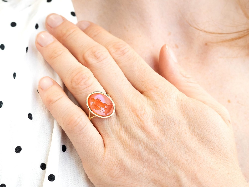 An antique 9ct yellow gold ring featuring an oval carved orange agate intaglio depicting a figure with split shoulders. View IV