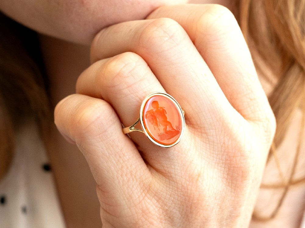 An antique 9ct yellow gold ring featuring an oval carved orange agate intaglio depicting a figure with split shoulders. View V
