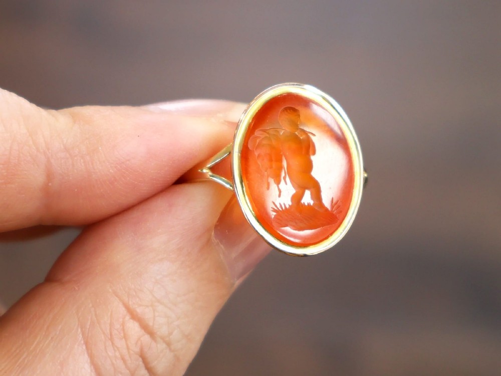 An antique 9ct yellow gold ring featuring an oval carved orange agate intaglio depicting a figure with split shoulders. View VI
