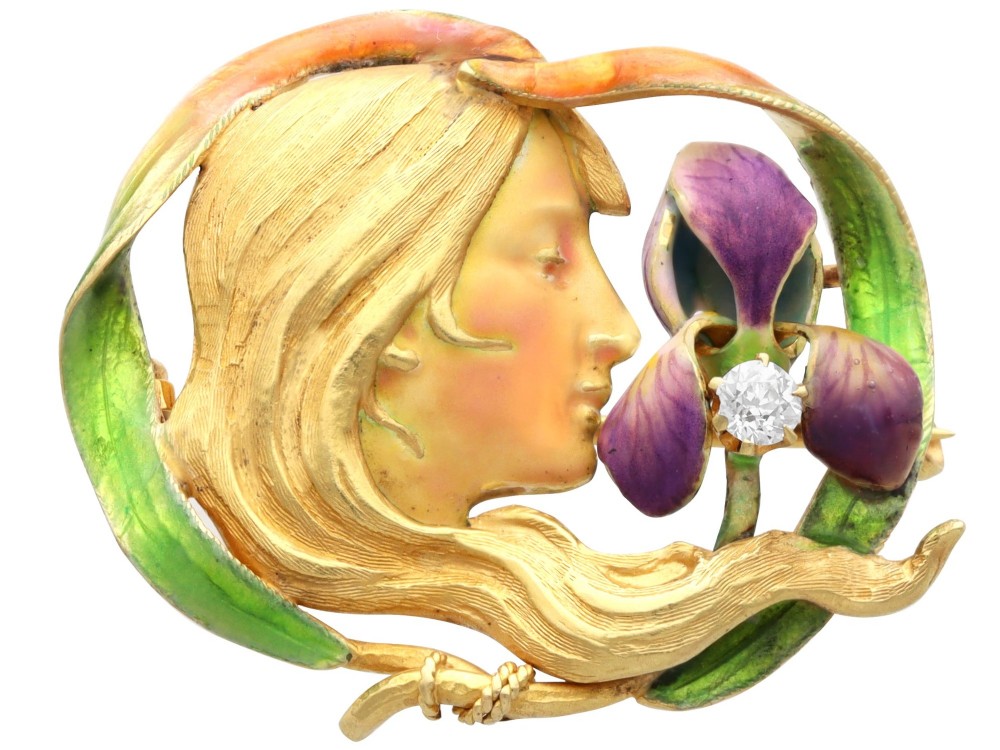 An Art Nouveau 18ct yellow gold brooch detailing a maiden profile framed by green enamel foliage and a purple enamelled iris set with a single diamond.