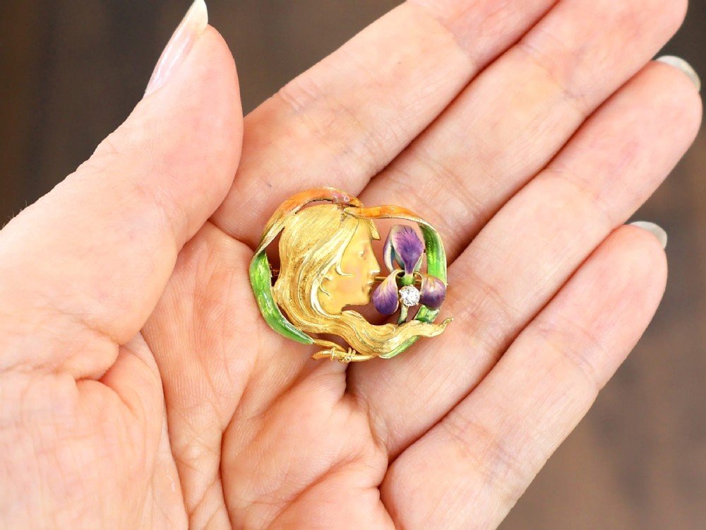 An Art Nouveau 18ct yellow gold brooch detailing a maiden profile framed by green enamel foliage and a purple enamelled iris set with a single diamond. View IV