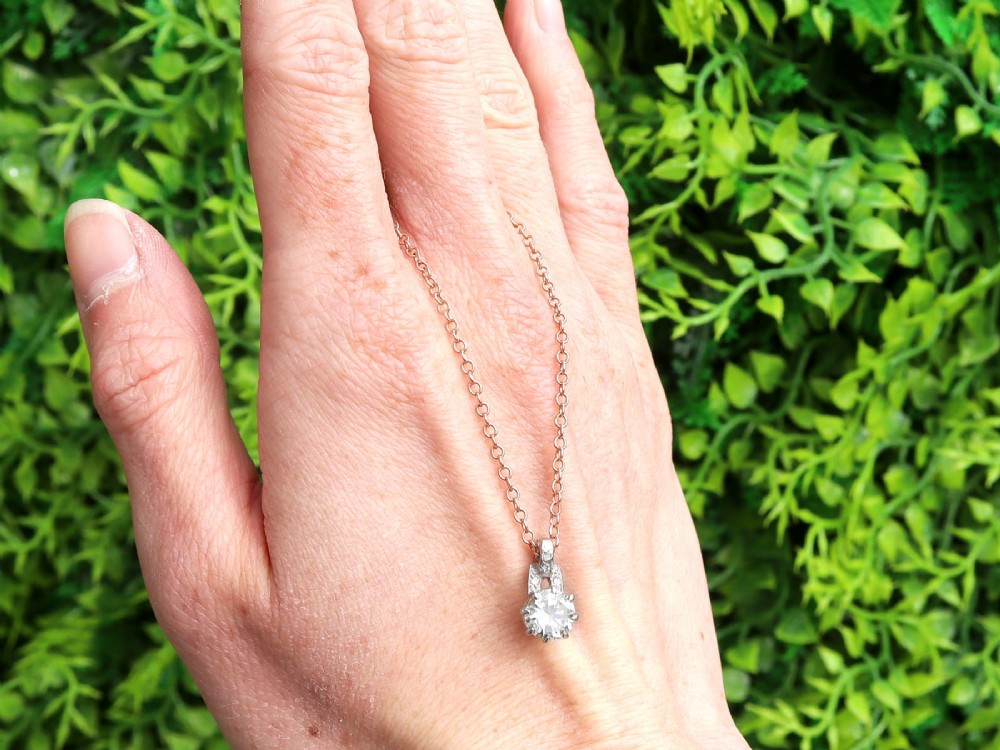 An antique platinum solitaire pendant featuring a round diamond in a claw setting suspended from a fine gold chain. View II