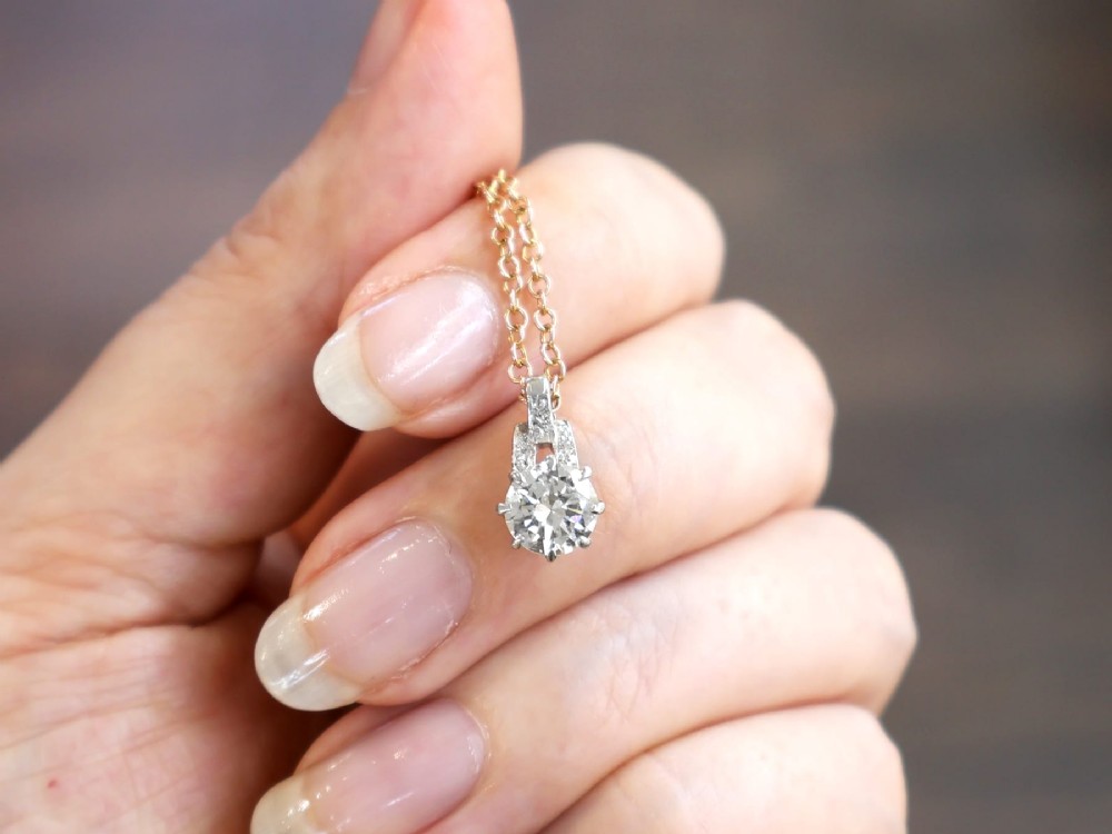 An antique platinum solitaire pendant featuring a round diamond in a claw setting suspended from a fine gold chain. View III