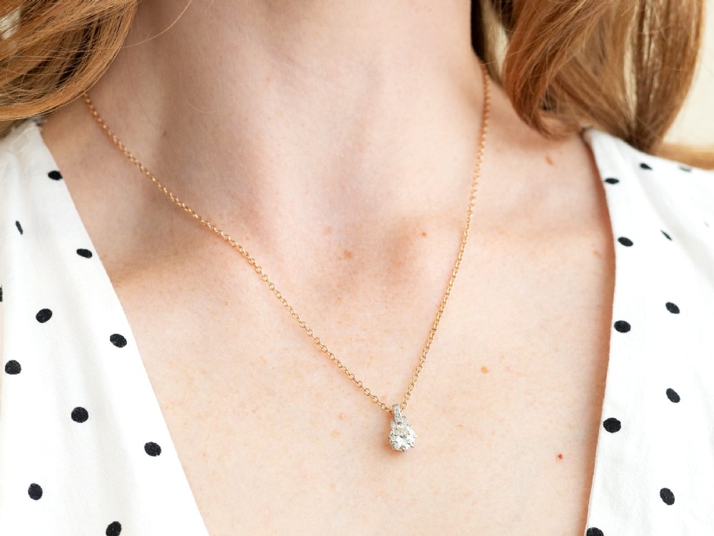 An antique platinum solitaire pendant featuring a round diamond in a claw setting suspended from a fine gold chain. View IX
