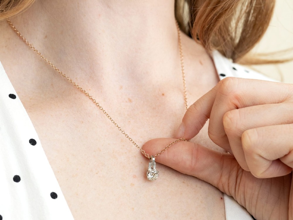 An antique platinum solitaire pendant featuring a round diamond in a claw setting suspended from a fine gold chain. View X