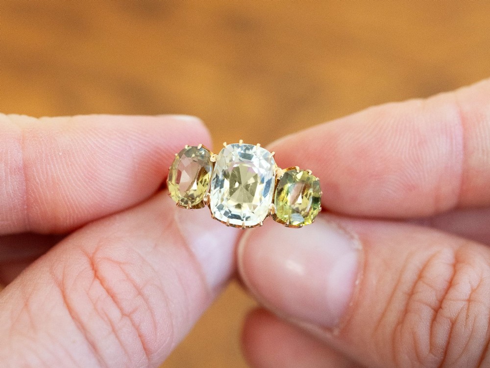 A late Victorian 18ct yellow gold trilogy ring featuring a central cushion-cut yellow sapphire flanked by two greenish-yellow chrysoberyl gemstones in claw settings. View III