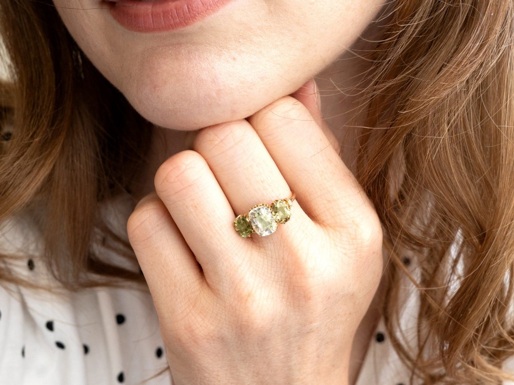 A late Victorian 18ct yellow gold trilogy ring featuring a central cushion-cut yellow sapphire flanked by two greenish-yellow chrysoberyl gemstones in claw settings. View IV