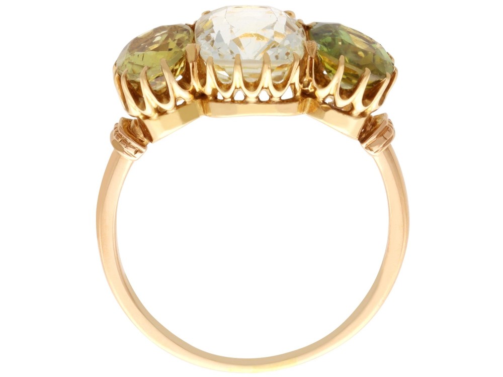 A late Victorian 18ct yellow gold trilogy ring featuring a central cushion-cut yellow sapphire flanked by two greenish-yellow chrysoberyl gemstones in claw settings. View IX