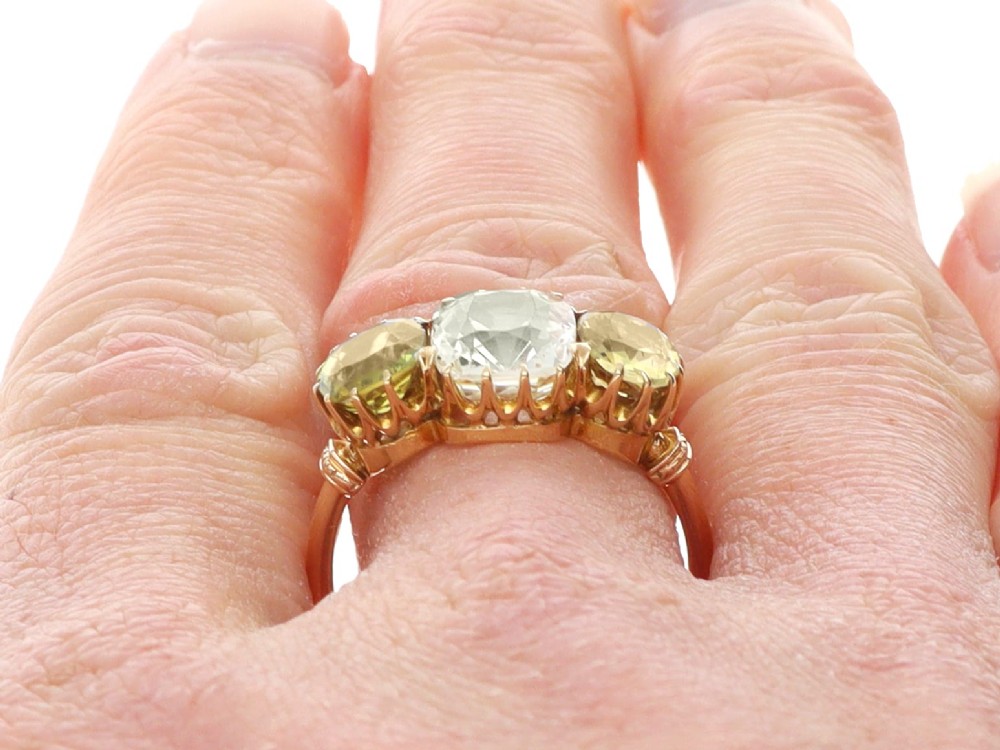 A late Victorian 18ct yellow gold trilogy ring featuring a central cushion-cut yellow sapphire flanked by two greenish-yellow chrysoberyl gemstones in claw settings. View XIII