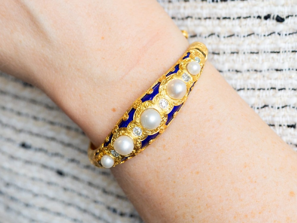 A Victorian hinged yellow gold bangle featuring detailed hand engraving, deep blue enamel panels, set diamonds, and graduated natural pearls. View III