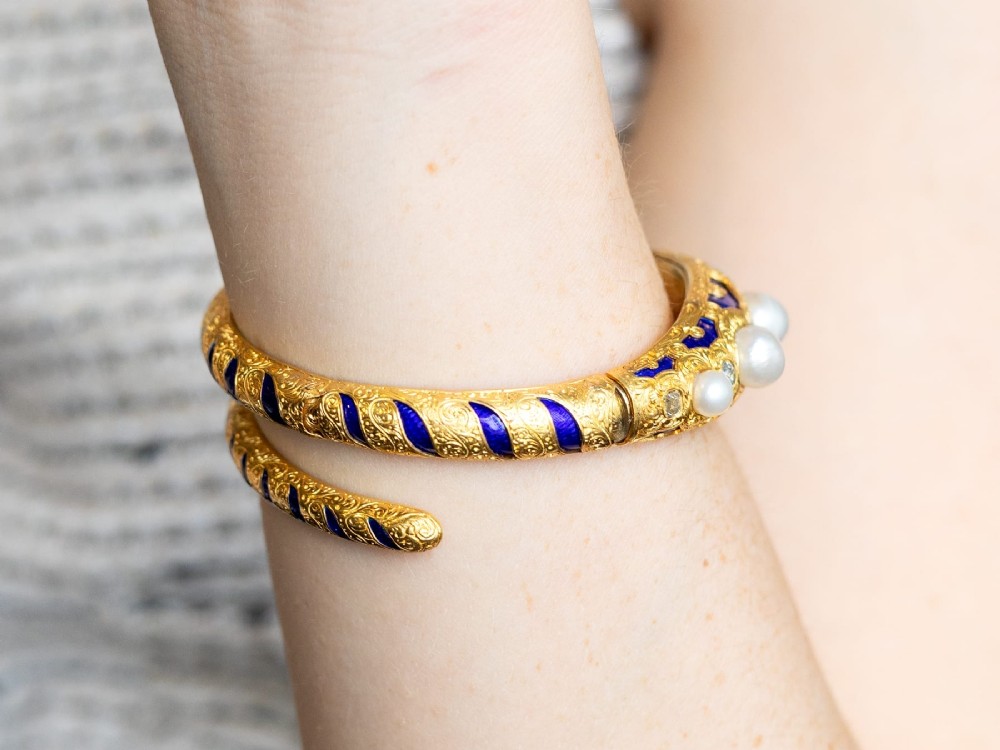A Victorian hinged yellow gold bangle featuring detailed hand engraving, deep blue enamel panels, set diamonds, and graduated natural pearls. View IV