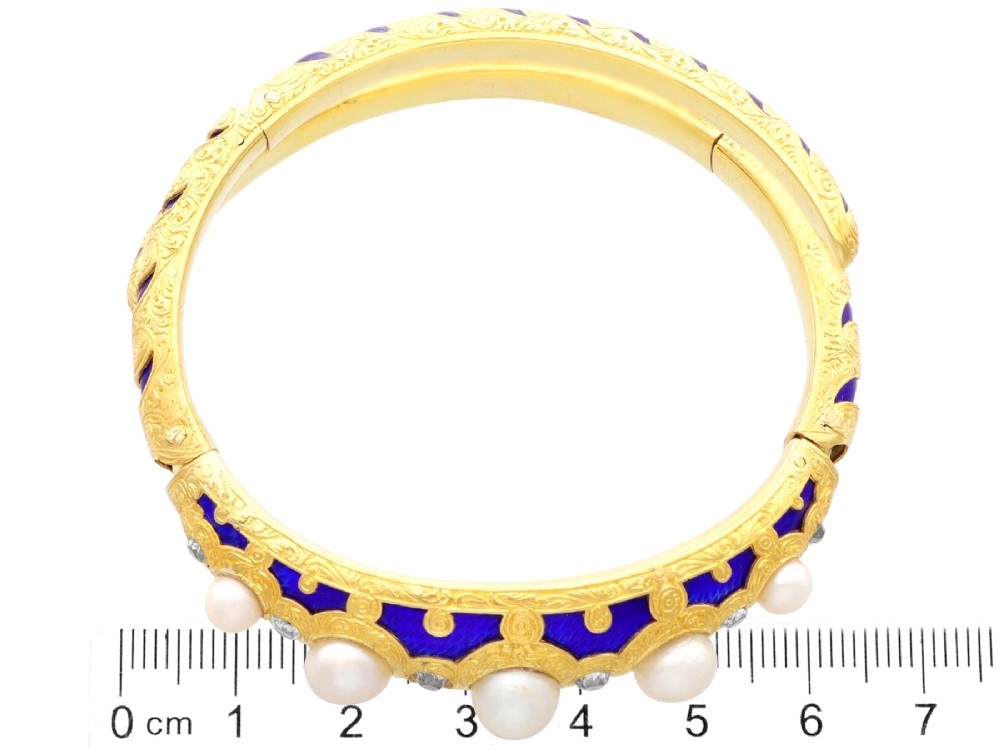 A Victorian hinged yellow gold bangle featuring detailed hand engraving, deep blue enamel panels, set diamonds, and graduated natural pearls. View XI