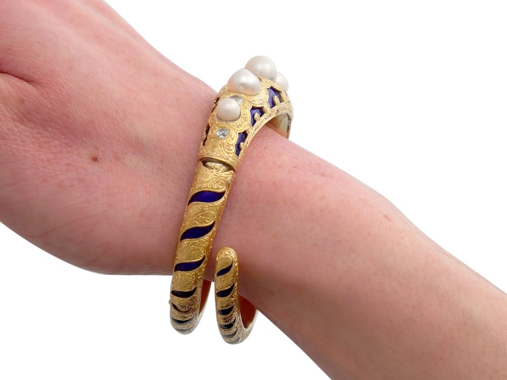 A Victorian hinged yellow gold bangle featuring detailed hand engraving, deep blue enamel panels, set diamonds, and graduated natural pearls. View XII