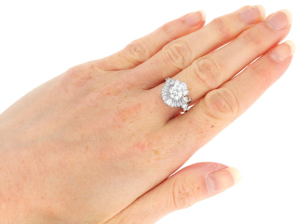 An 18ct white gold Art Deco cocktail ring featuring a central round diamond surrounded by a fan of baguette diamonds and accent round diamonds. View X