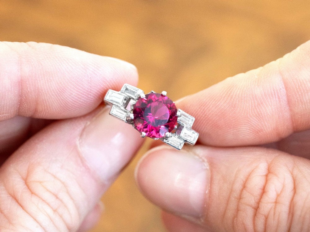 An Art Deco platinum ring featuring a round pink tourmaline centre stone set between stepped shoulders of baguette-cut diamonds. View III