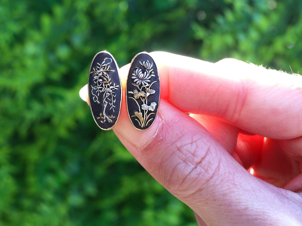 A pair of late nineteenth-century double-ended oval cufflinks crafted in 18ct yellow gold, featuring dark patinated shakudo panels with gold and silver botanical relief inlays. View II