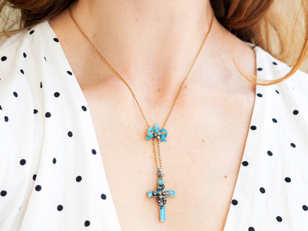 A Georgian 15ct yellow gold cross pendant featuring blue enamel, a diamond-set ribbon bow loop, and floral diamond overlays. View V