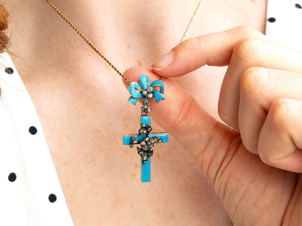 A Georgian 15ct yellow gold cross pendant featuring blue enamel, a diamond-set ribbon bow loop, and floral diamond overlays. View VI