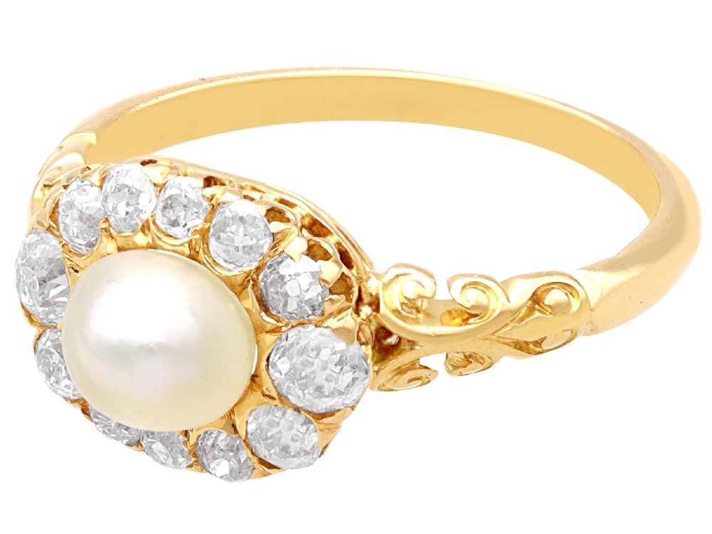 An 18ct yellow gold cluster ring featuring a central oval natural pearl surrounded by a halo of old-cut diamonds with scroll-carved shoulders. View VI