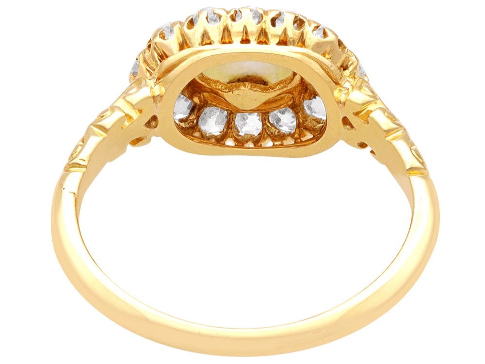 An 18ct yellow gold cluster ring featuring a central oval natural pearl surrounded by a halo of old-cut diamonds with scroll-carved shoulders. View VII