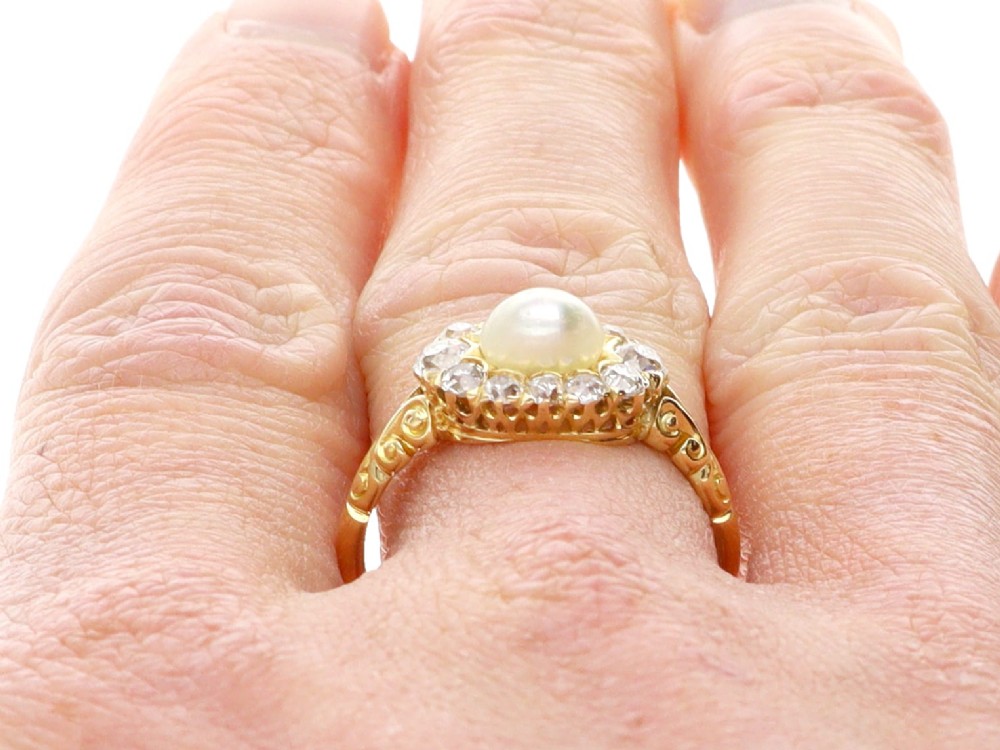 An 18ct yellow gold cluster ring featuring a central oval natural pearl surrounded by a halo of old-cut diamonds with scroll-carved shoulders. View XII