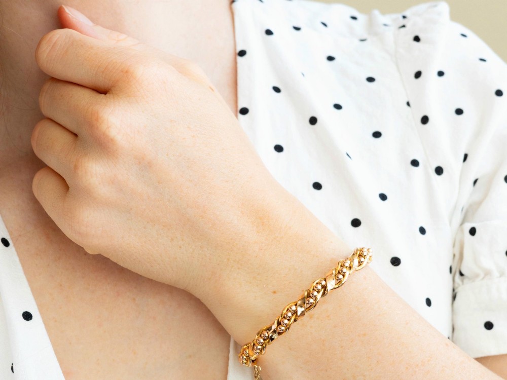 An antique Edwardian 15ct gold hinged bangle featuring a twisted ribbon design intertwined around a row of polished gold beads, fitted with a safety chain. View V