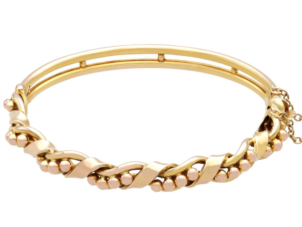 An antique Edwardian 15ct gold hinged bangle featuring a twisted ribbon design intertwined around a row of polished gold beads, fitted with a safety chain. View VII