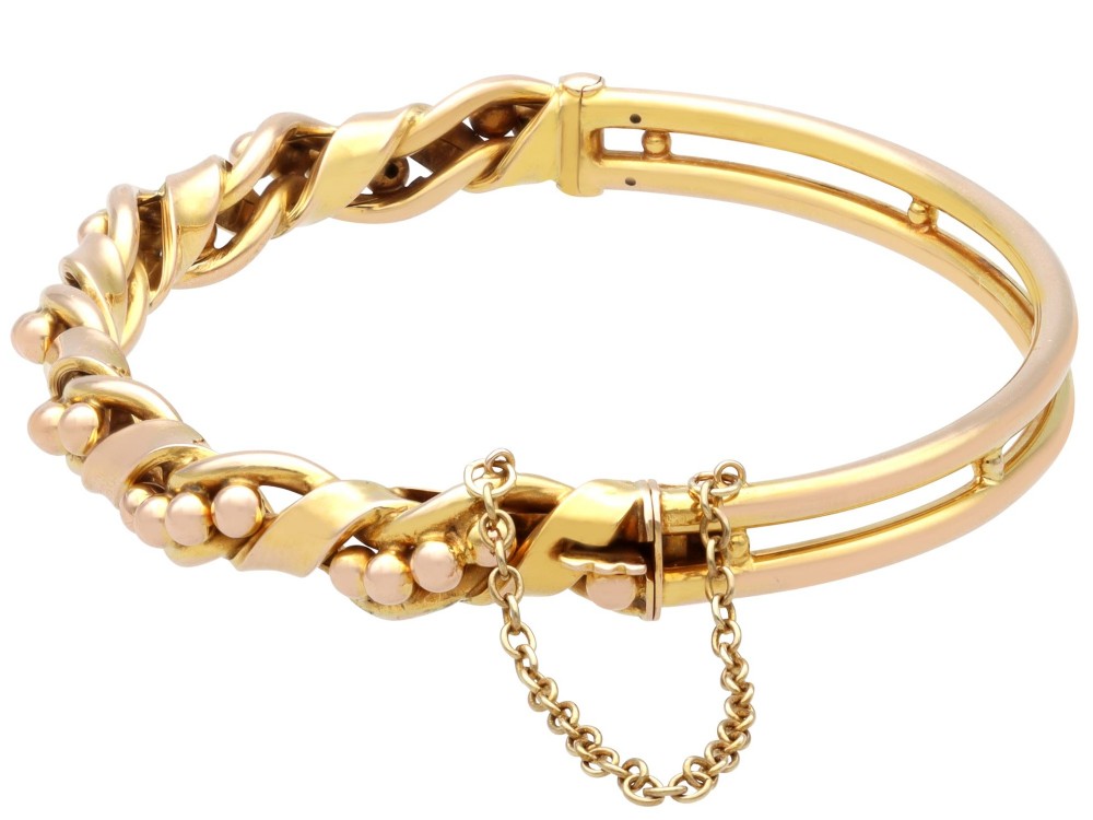 An antique Edwardian 15ct gold hinged bangle featuring a twisted ribbon design intertwined around a row of polished gold beads, fitted with a safety chain. View VIII