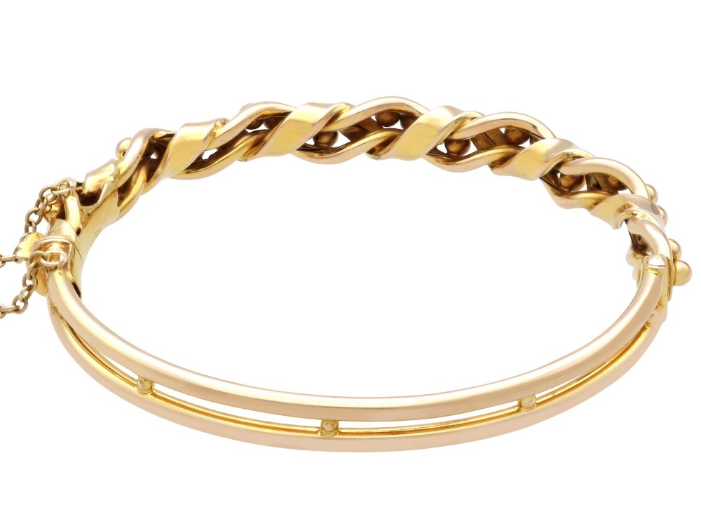 An antique Edwardian 15ct gold hinged bangle featuring a twisted ribbon design intertwined around a row of polished gold beads, fitted with a safety chain. View IX