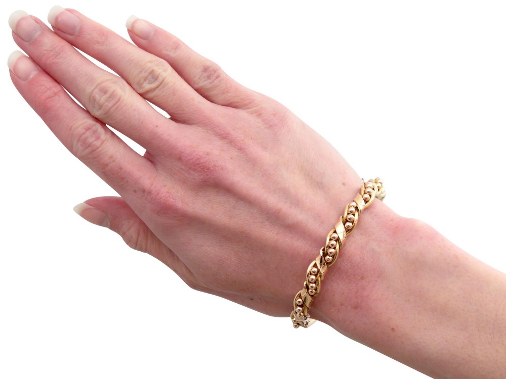 An antique Edwardian 15ct gold hinged bangle featuring a twisted ribbon design intertwined around a row of polished gold beads, fitted with a safety chain. View XIII