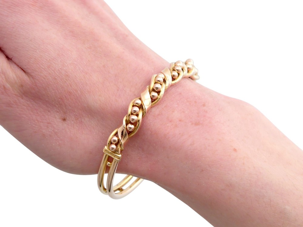 An antique Edwardian 15ct gold hinged bangle featuring a twisted ribbon design intertwined around a row of polished gold beads, fitted with a safety chain. View XIV
