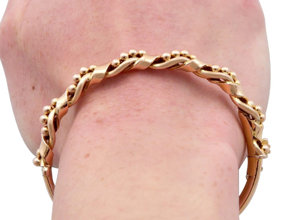 An antique Edwardian 15ct gold hinged bangle featuring a twisted ribbon design intertwined around a row of polished gold beads, fitted with a safety chain. View XV