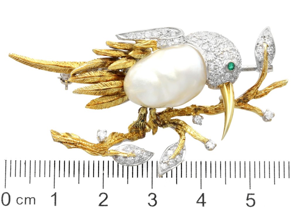 An antique 14ct gold bird brooch featuring a blister pearl body, pave diamond head with an emerald eye, perched on a textured gold branch. View X