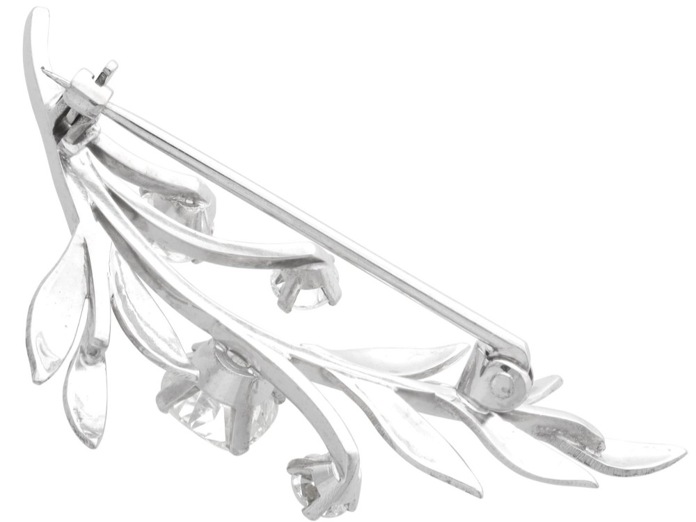 An 18ct white gold brooch crafted in the shape of a flowering spray, featuring leaf motifs and claw-set diamonds. View VI