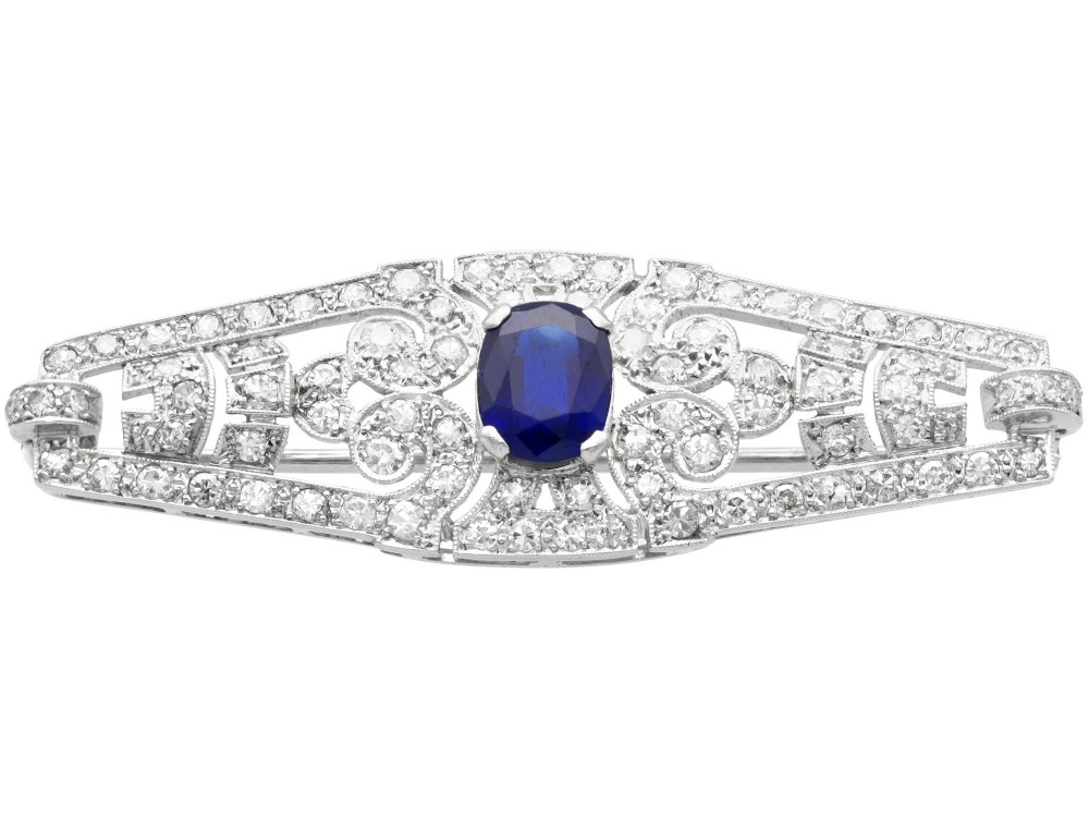 An Art Deco 9ct white gold brooch featuring a central oval blue sapphire framed by geometric openwork set with round diamonds.
