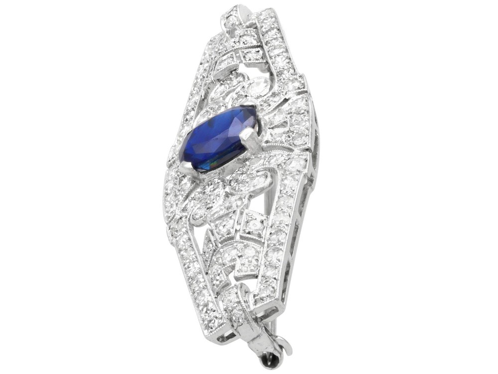 An Art Deco 9ct white gold brooch featuring a central oval blue sapphire framed by geometric openwork set with round diamonds. View VI