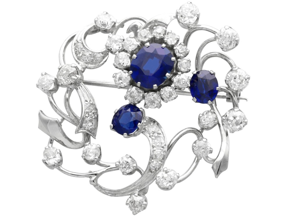 An Edwardian 18ct white gold brooch set with three oval blue sapphires surrounded by openwork diamond-set scrollwork.